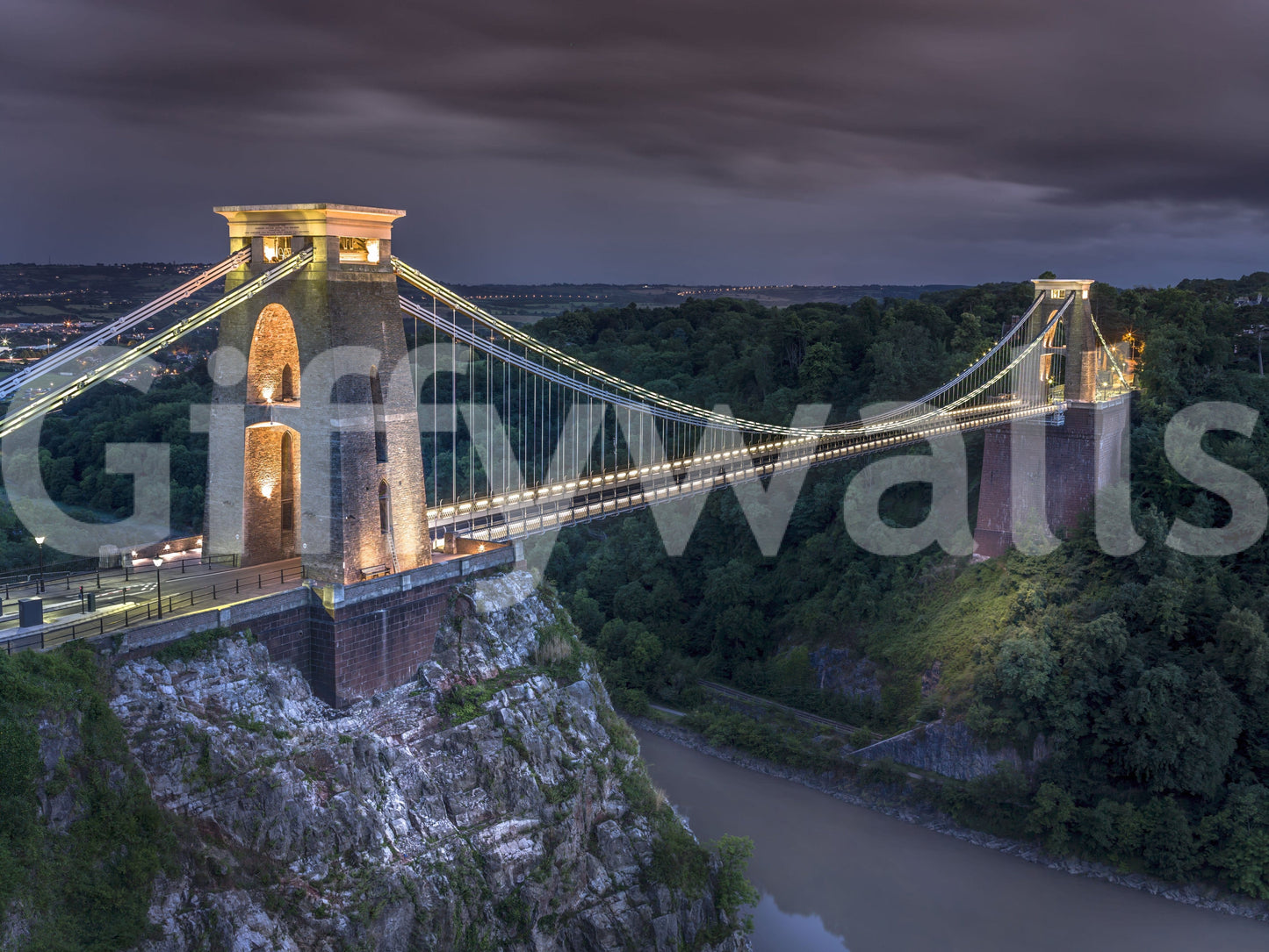 Glowing arches of Clifton Suspension Bridge against dark sky.