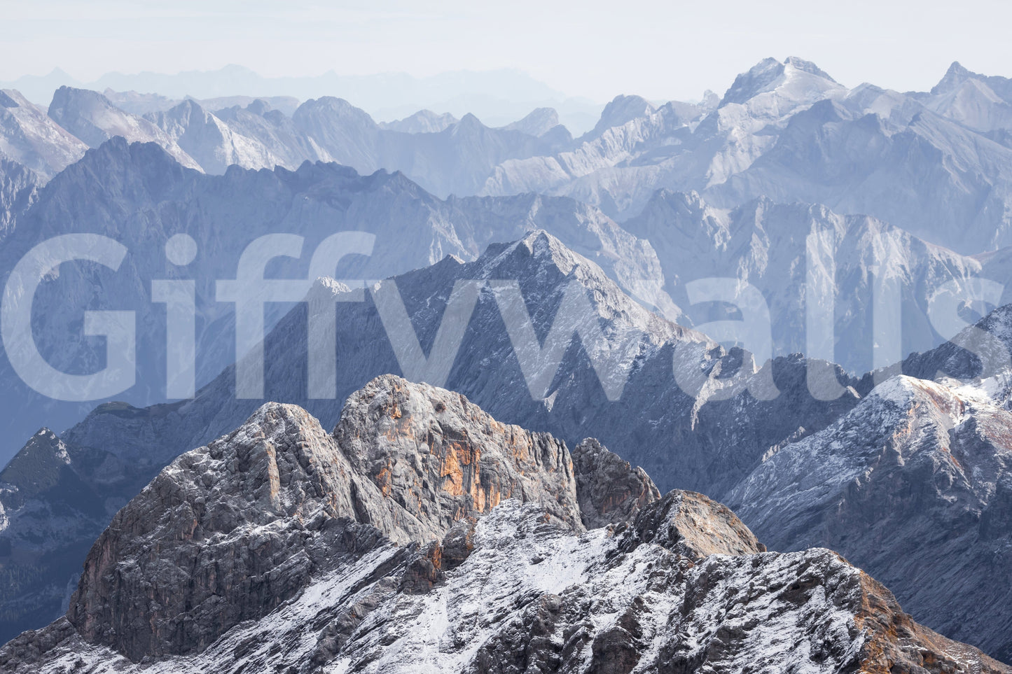 Ethereal Range wallpaper shown as a full-wall mural of hazy blue mountain ranges with a snow-dusted rocky summit