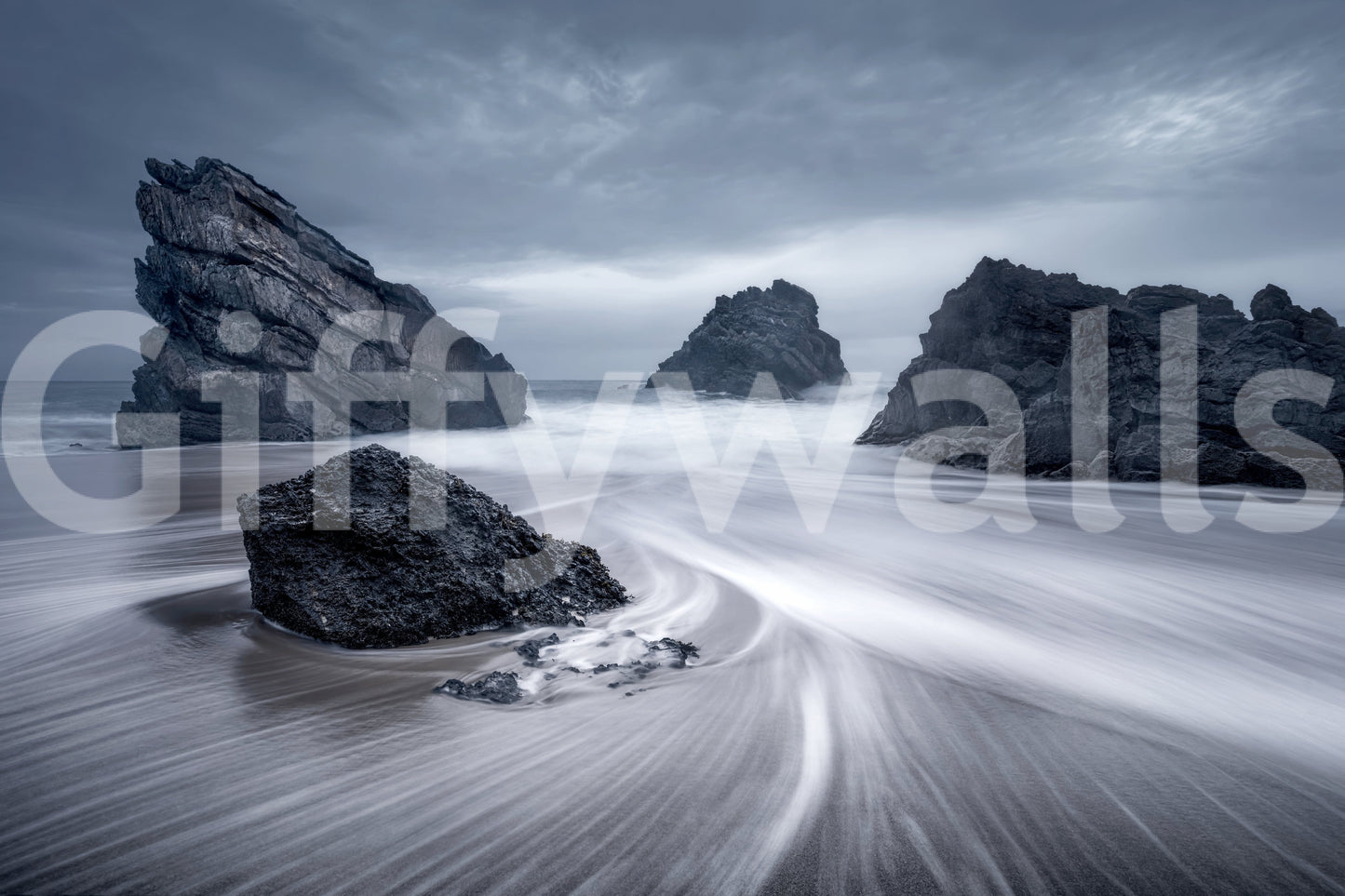 Coastal Monoliths wallpaper mural shown as a full-wall render of jagged dark sea stacks on a misty swirling beach