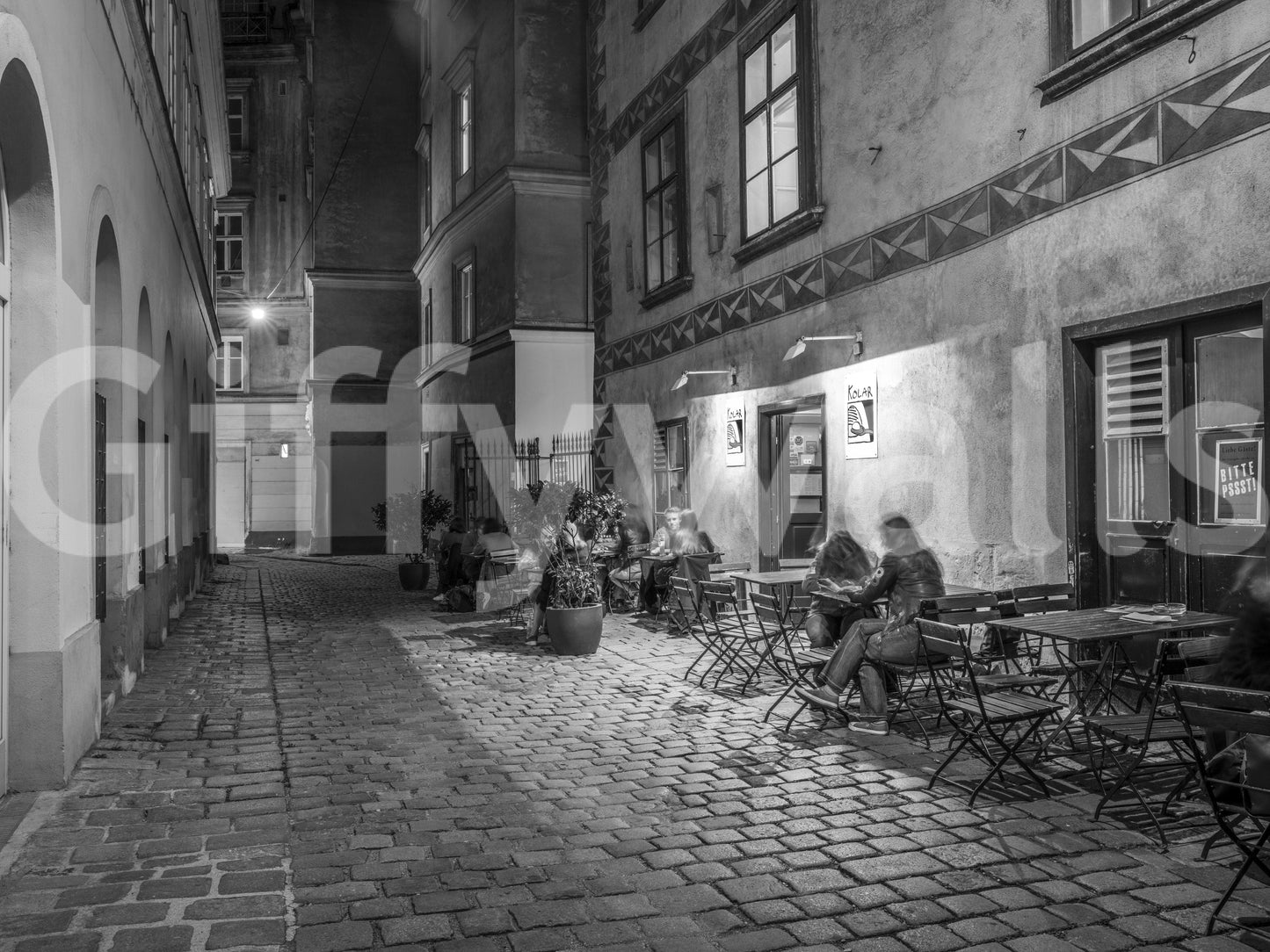 Street cafe in Vienna wallpaper mural close-up, black and white cobbled alley with diners at lamplit outdoor cafe tables