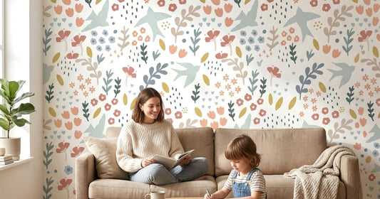 Mother and child relaxing on a beige sofa in front of a pastel spring wallpaper mural featuring birds, flowers, and leaves in soft pinks, blues, and greens