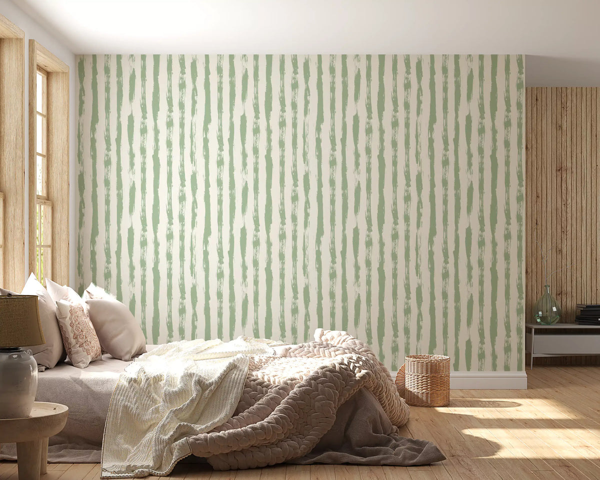 Sage brushstroke vertical stripes wallpaper on a bedroom accent wall above a bed with a knit throw GD12271