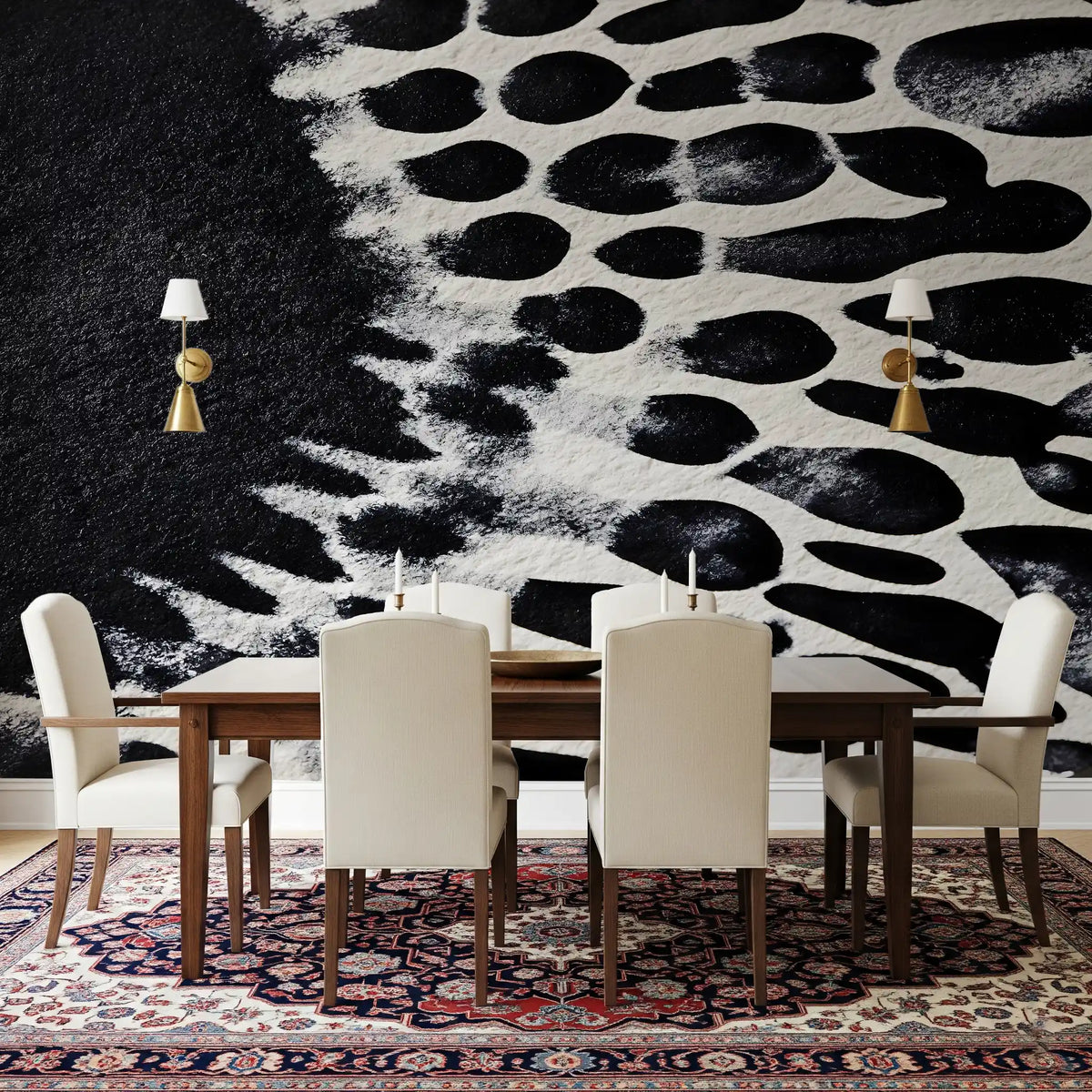 Black and white wallpaper of ink blots behind a dining table, cream chairs and brass sconces GD14167