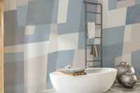 Abstract Cubist wallpaper mural of blue and beige blocks behind a white freestanding tub and towel ladder