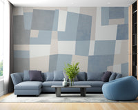 Abstract Cubist wallpaper mural in blue and beige geometric blocks behind a blue-grey sectional and beanbag