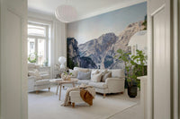 Alpine Reflections wallpaper mural of grey mountains and forest behind a cream sofa in a Scandinavian living room