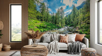 Alpine Stream wallpaper mural with a forest creek behind a cream sofa and wood-slat wall in a living room