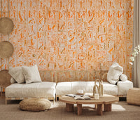 Ancient Inscriptions wallpaper mural in orange hieroglyphics behind an off-white sectional sofa in a sunlit living room