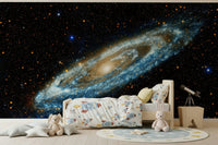 Andromeda galaxy mural in blue and gold above a wooden kids bed with rocket bedding and a telescope