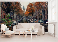 Autumn Canal Charm wallpaper mural of an autumn canal behind a cream sofa and wood-frame armchair in a living room