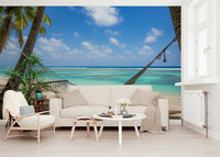 Beach Hammock Haven wallpaper mural of palms and lagoon behind a cream sofa and white rattan armchair in a living room