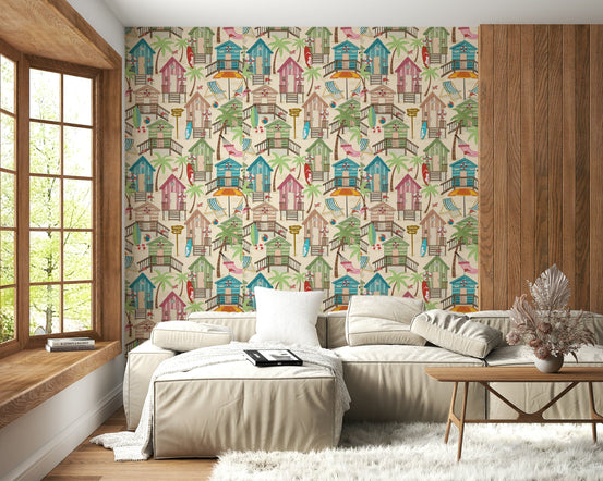 Beach Huts Bliss wallpaper with colourful seaside cabins behind a beige sectional sofa in a cosy living room