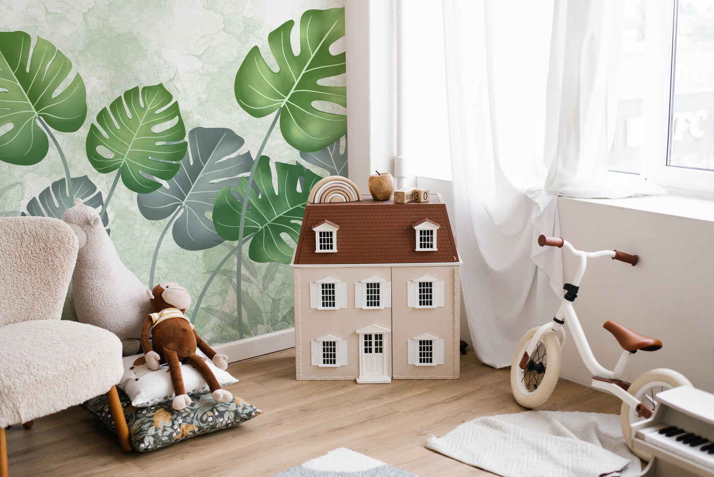 Best Tropical Wild Trees wallpaper mural with green leaves behind a boucle armchair and toy dollhouse in a kids room