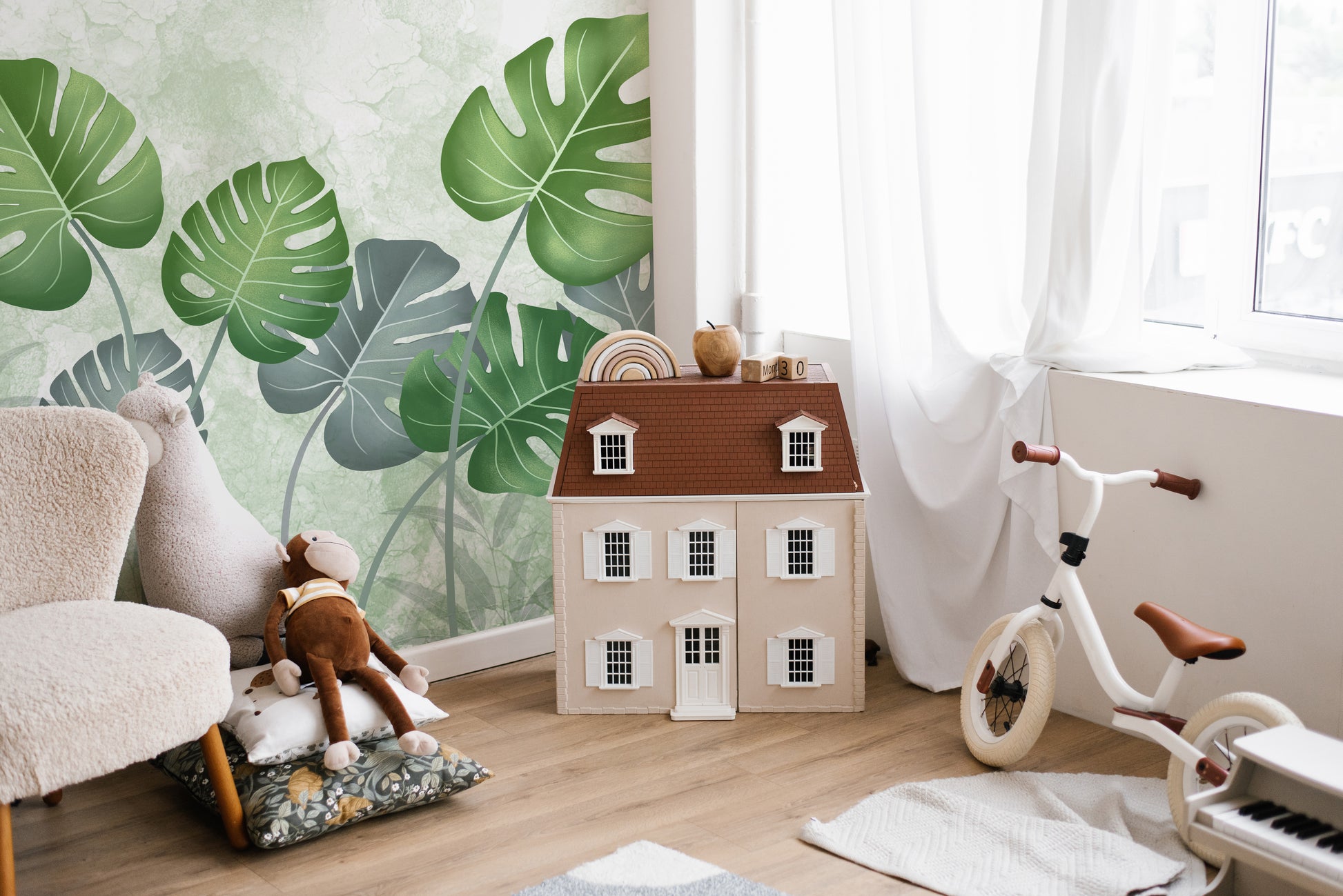 Best Tropical Wild Trees wallpaper mural with green leaves behind a boucle armchair and toy dollhouse in a kids room