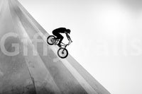 Biker wall mural in black and white showing a BMX rider speeding down a steep wooden ramp against a pale sky