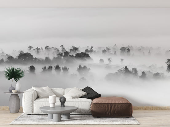 Black and white Clouds over Forest wallpaper mural of misty treetops behind a cream sofa and brown leather ottoman