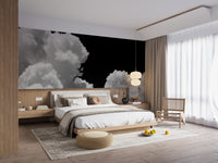 Black and white Clouds mural of white clouds on black above a low wood bed with beige bedding and a rattan chair