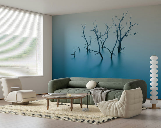 Aqua Reflections mural of bare branches in teal water behind a sage-green sofa and white chair in a living room