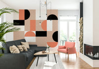 Blush Geometry wallpaper mural behind a charcoal sofa and coral armchair beside a firewood-stacked fireplace