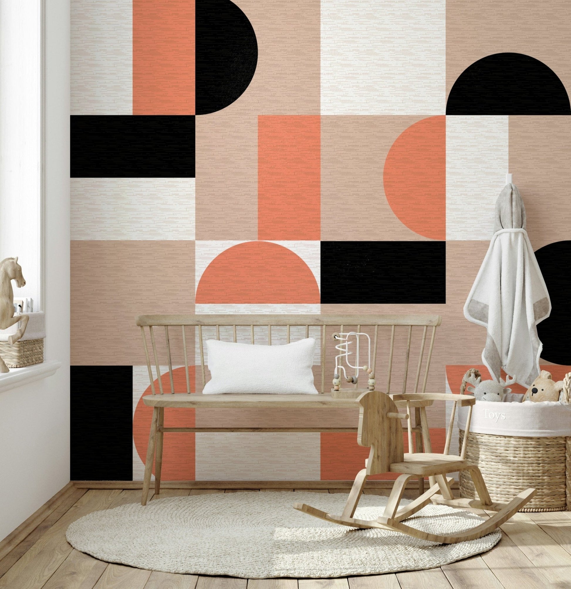 Blush Geometry wallpaper mural in orange, black and blush shapes behind a wooden bench in a nursery corner