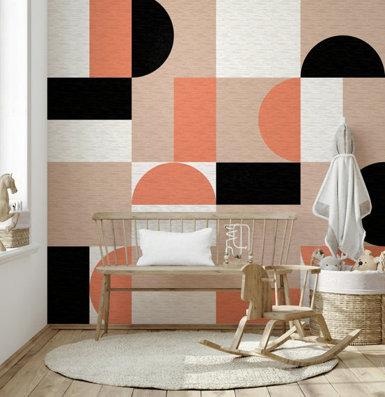 Blush Geometry wallpaper mural in orange, black and blush shapes behind a wooden bench in a nursery corner