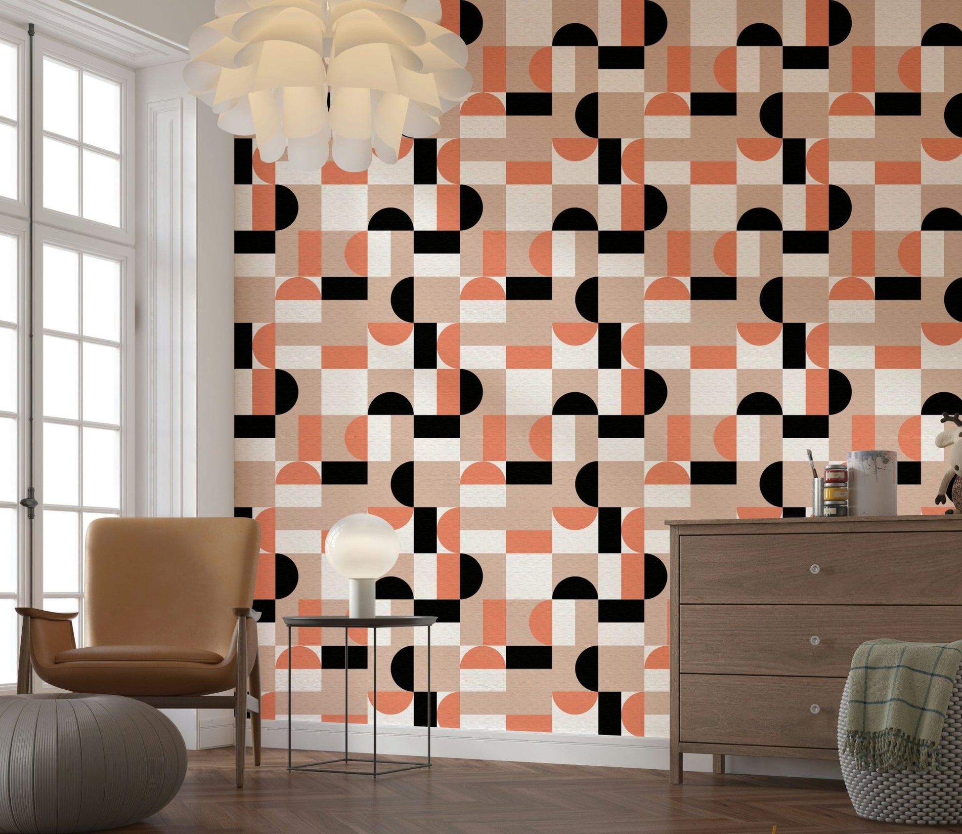 Blush Geometry wallpaper in pink, coral and black behind a tan armchair and knit pouf in a bright living room