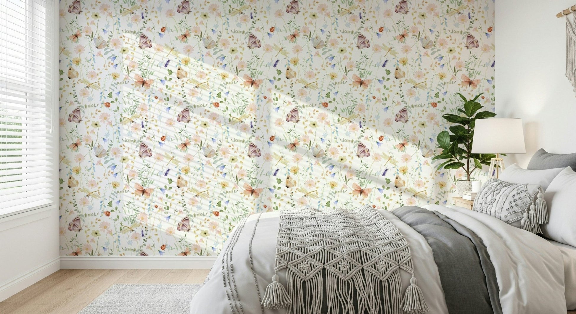 Blush Meadow's Whisper wallpaper of soft florals and butterflies behind a bed with a grey macrame throw in a bedroom