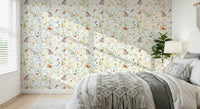 Blush Meadow's Whisper wallpaper of soft florals and butterflies behind a bed with a grey macrame throw in a bedroom