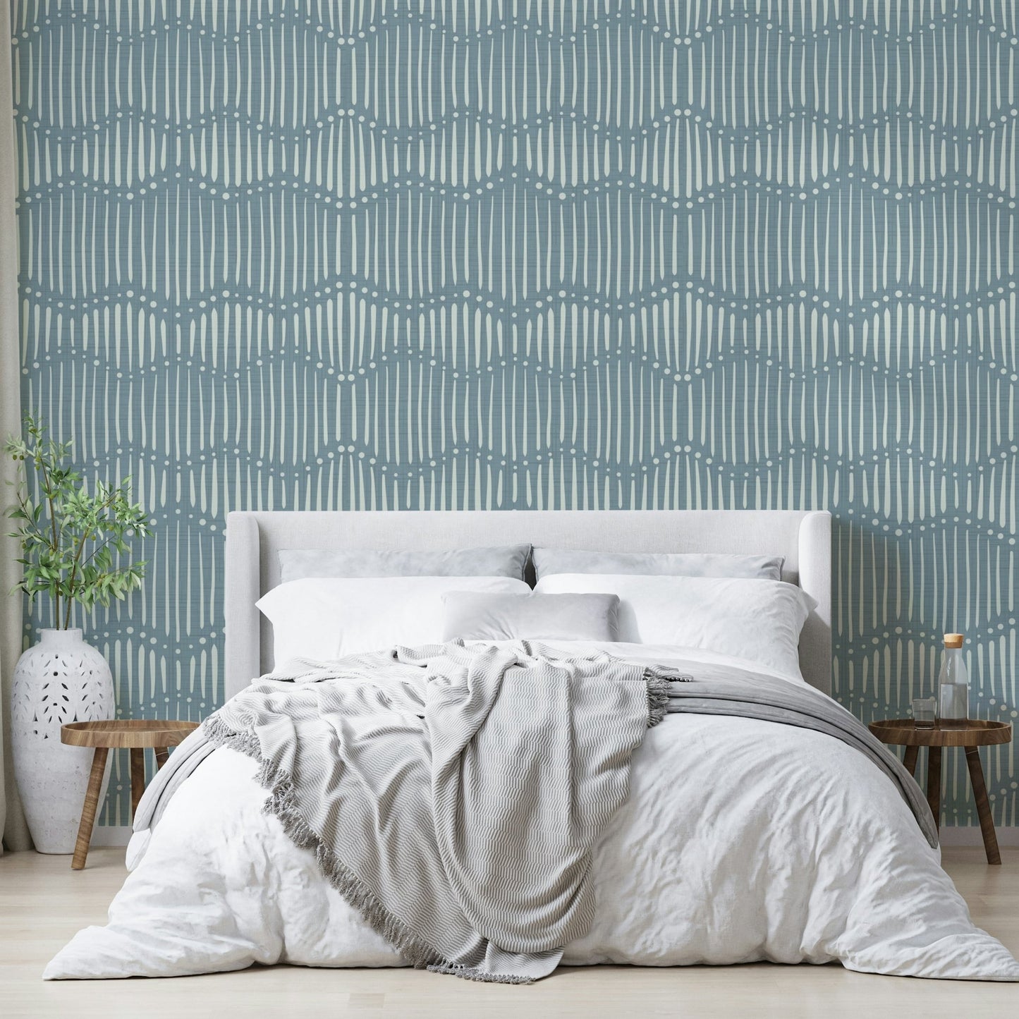 Boho Waves On Arona Canvas wallpaper in dusty blue behind a white upholstered bed with grey throw and white vase