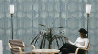 Boho Waves On Arona Canvas wallpaper in slate blue with cream dash lines behind a woman seated in a lounge with floor lamps