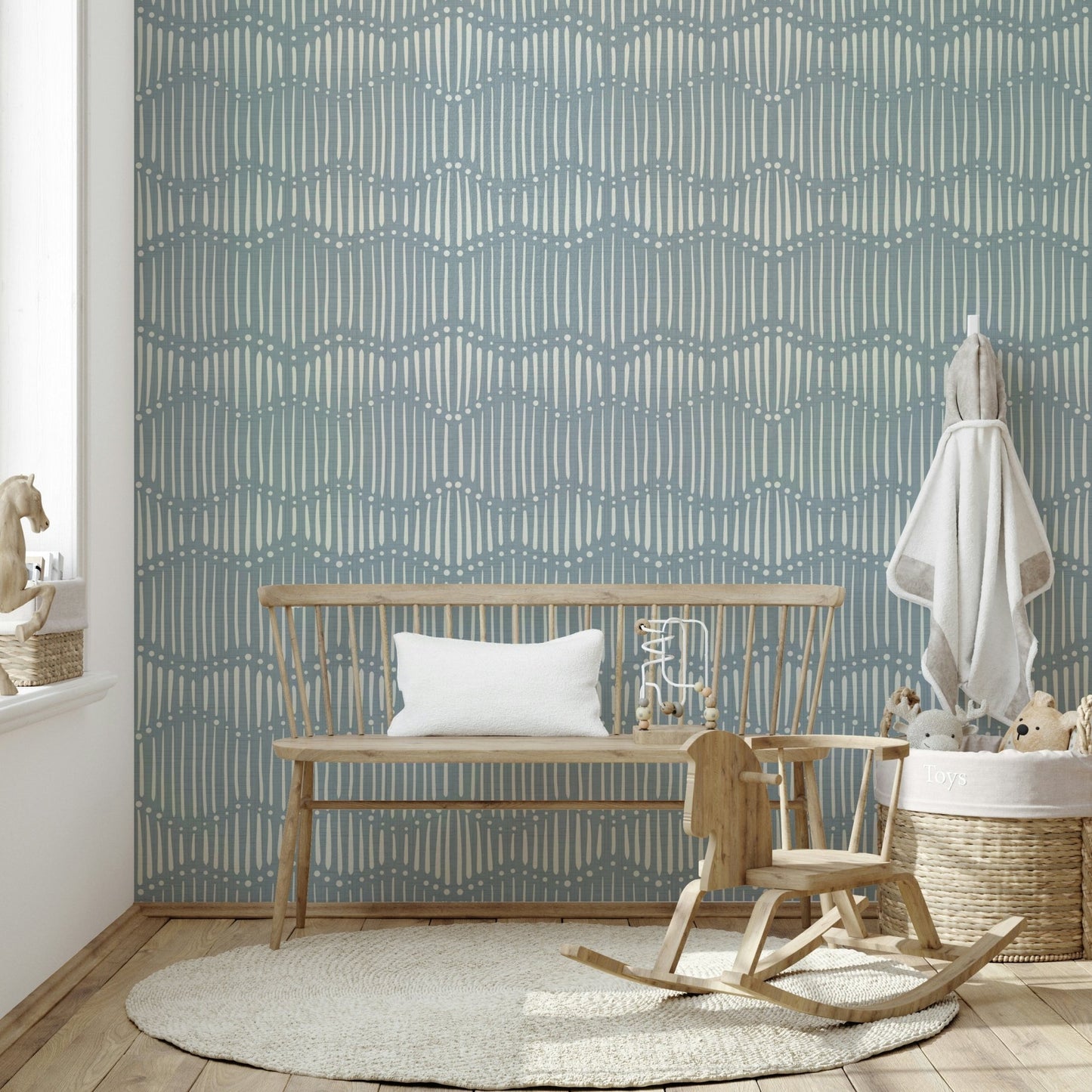 Boho Waves On Arona Canvas wallpaper in soft blue in a nursery with a wooden bench, rocking horse and toy basket
