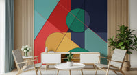 Bold Bauhaus wallpaper mural of bright shapes behind a white sideboard and two woven-back chairs