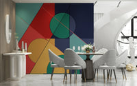 Bold Bauhaus wallpaper mural of red, teal and navy geometric shapes behind a round dining table and grey chairs