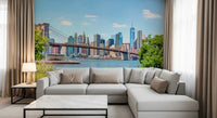 Bridge to Manhattan wall mural of the bridge and skyline behind a grey sectional sofa framed by beige curtains