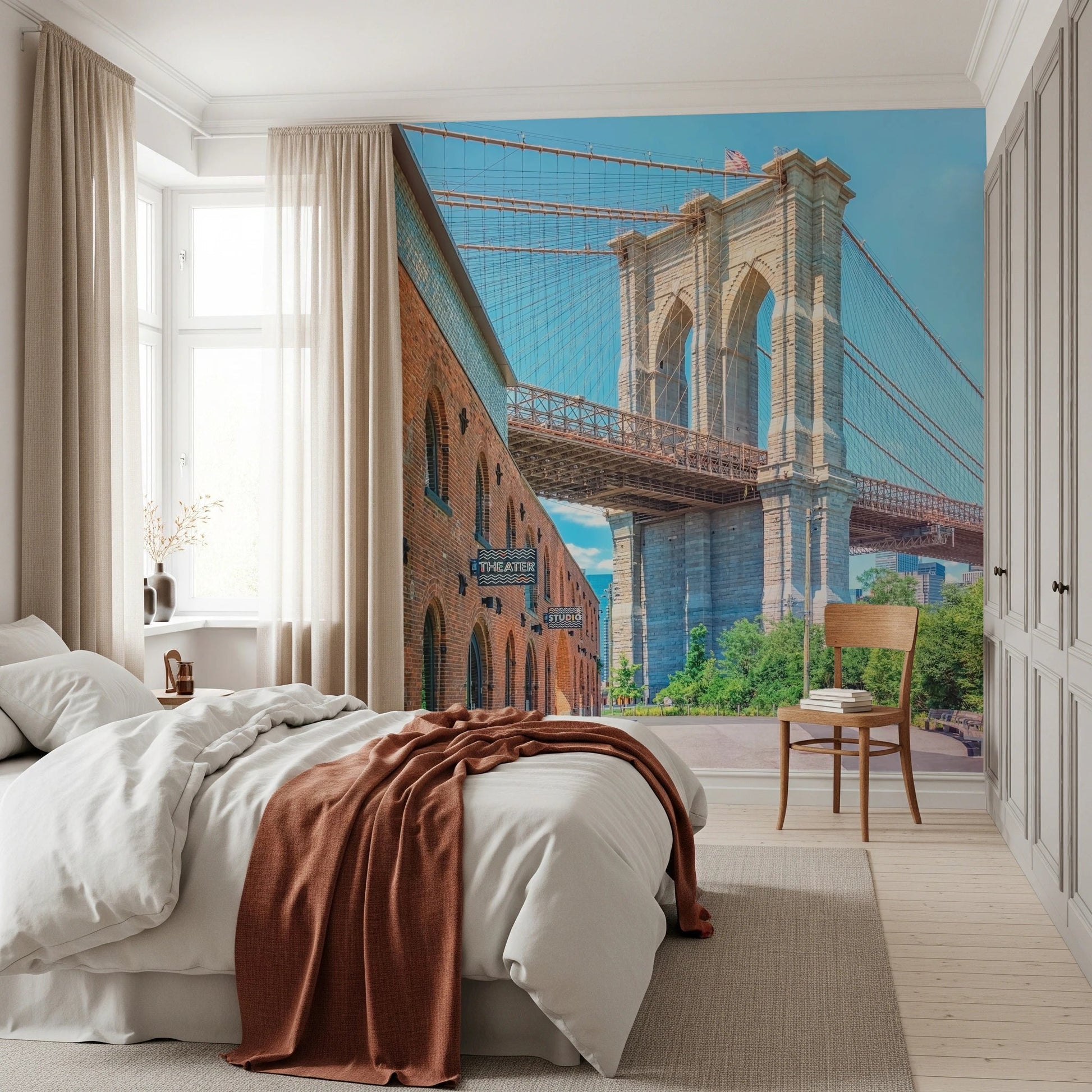 Brooklyn Bridge Vista wallpaper mural with the bridge tower behind a white bed and rust throw in a bright bedroom