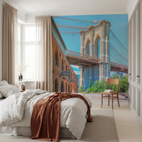 Brooklyn Bridge Vista wallpaper mural with the bridge tower behind a white bed and rust throw in a bright bedroom