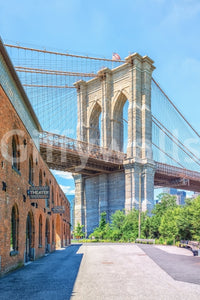 Brooklyn Bridge Vista wallpaper mural shown full-wall with the stone bridge tower, brick warehouse and riverside walkway