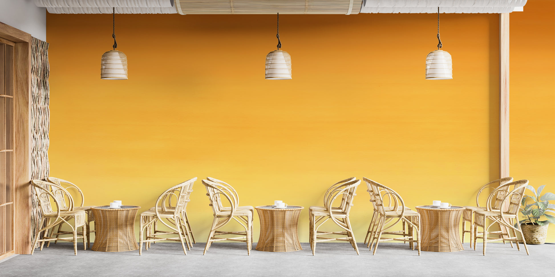 Honey Ombre wallpaper mural in warm yellow behind a row of rattan chairs and tables on a cafe terrace