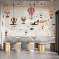 Whimsical Sky High Adventure wallpaper mural of hot air balloons and a plane behind rattan stools and tables in a cafe setting