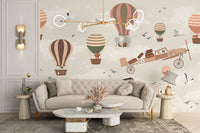Whimsical Sky High Adventure wallpaper mural with pastel balloons and a flying plane behind a beige tufted sofa in a living room