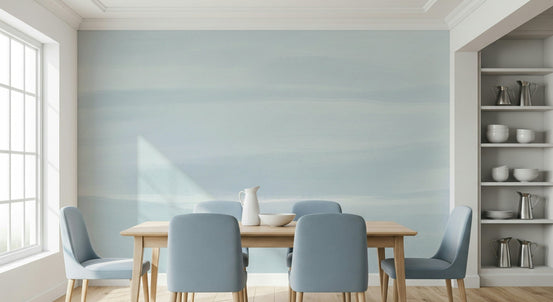 Serene Sky wallpaper mural of soft blue watercolor haze behind a wood dining table and dusty blue chairs