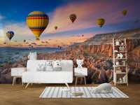Cappadocia Balloons Sunset wallpaper mural behind a white sofa with plush owl toys and a wooden shelf in a living room