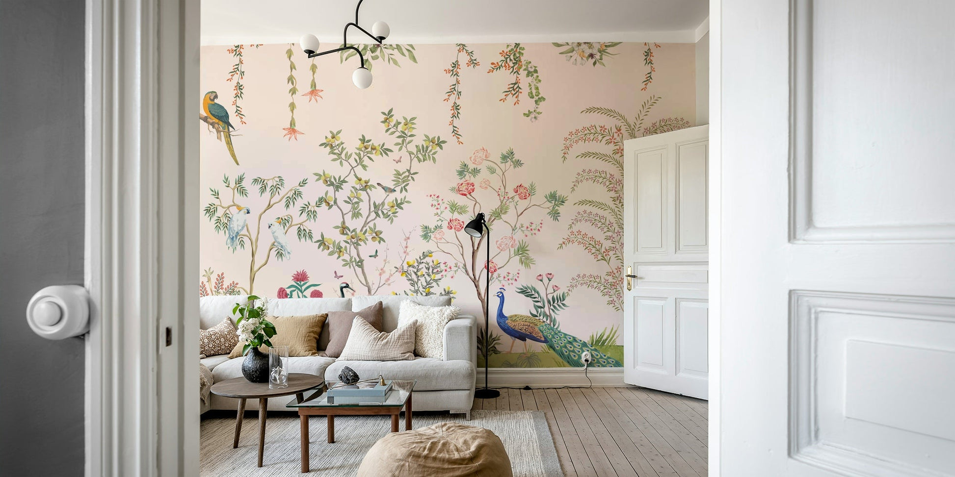 Chinoiserie Garden wallpaper mural with peacocks viewed through a doorway behind a white sofa in a living room