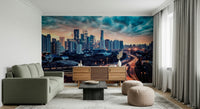 Cityscape Dawn wallpaper mural showing teal storm clouds over skyscrapers behind an olive sofa and wood credenza