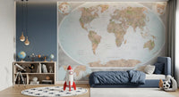 Classic world map in blue and earthy tones wallpaper mural behind a navy bed and rocket toy in a boys room