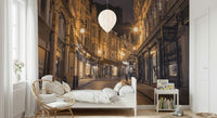 Cobblestone Street Nights wallpaper mural in a kids bedroom with white bed, rattan chair and balloon light