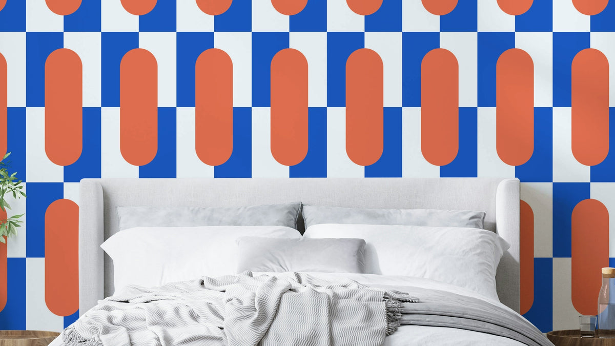 Coral Coast wallpaper with bold cobalt blue and orange capsule shapes behind a white upholstered bed in a bedroom