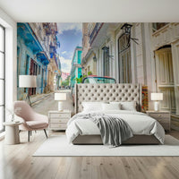 Cuban Classics wallpaper mural of a Havana street behind a tufted bed and pink chair in a bedroom