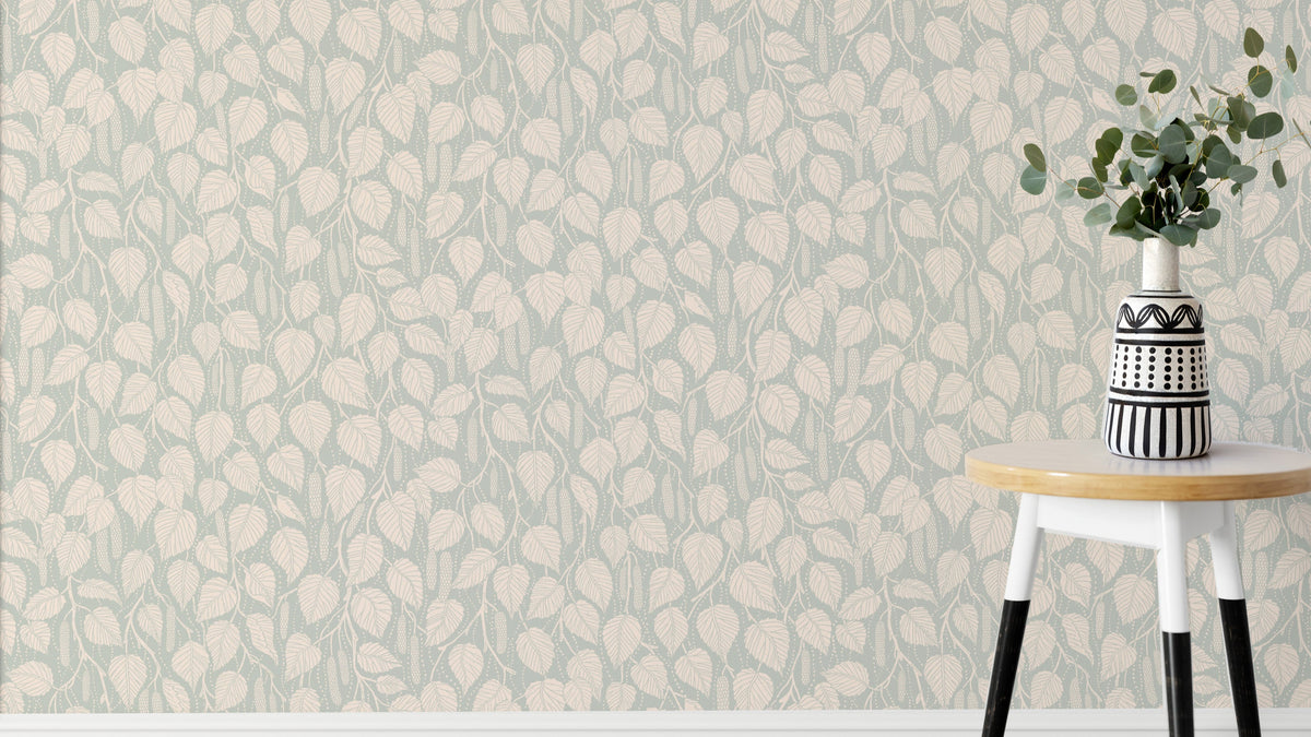 Dewy Birch Branches wallpaper in sage green behind a round stool with a striped vase and eucalyptus