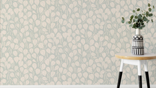 Dewy Birch Branches wallpaper in sage green behind a round stool with a striped vase and eucalyptus